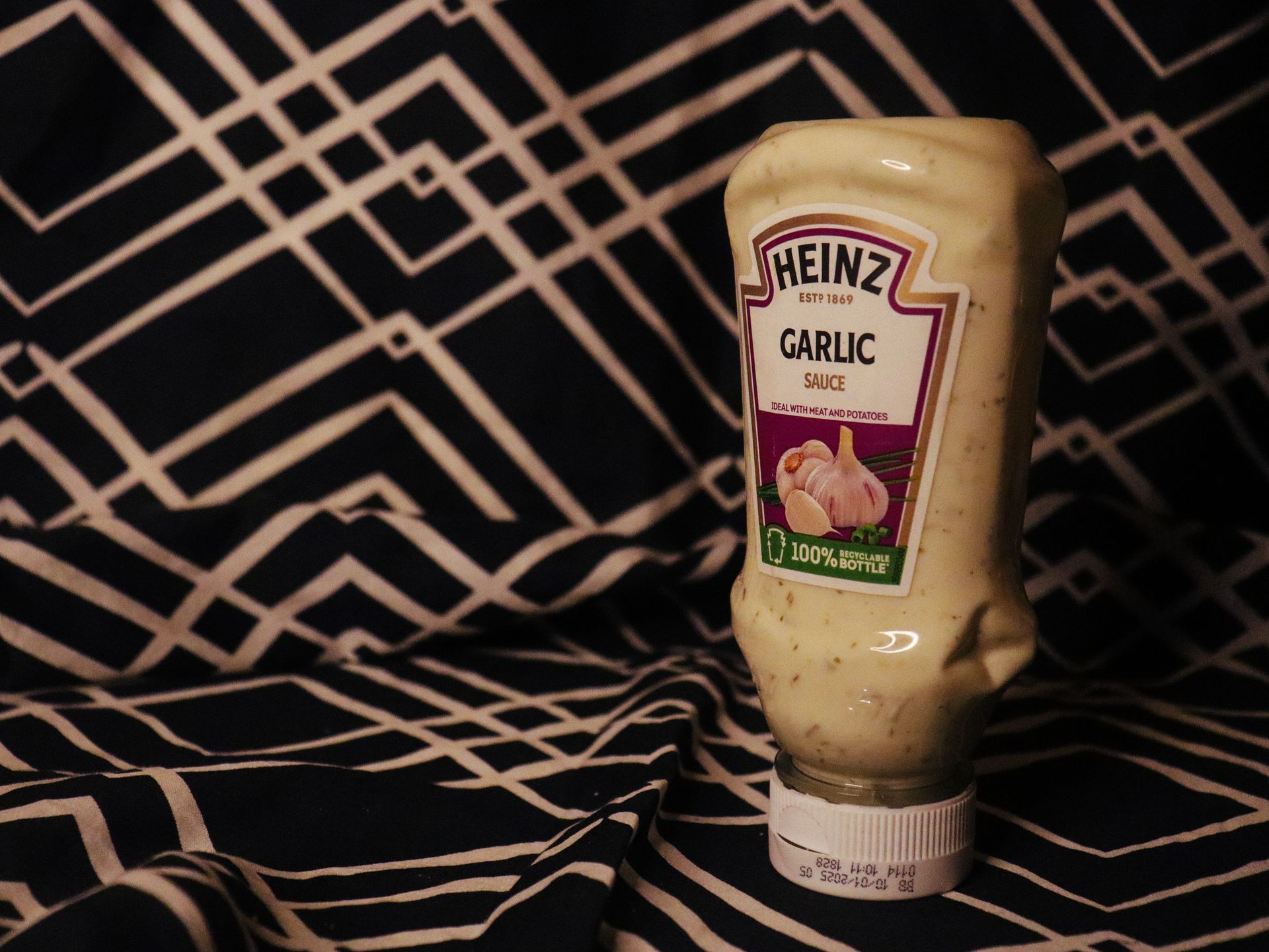 Heinz garlic sauce bottle on black and white geometric patterned fabric.