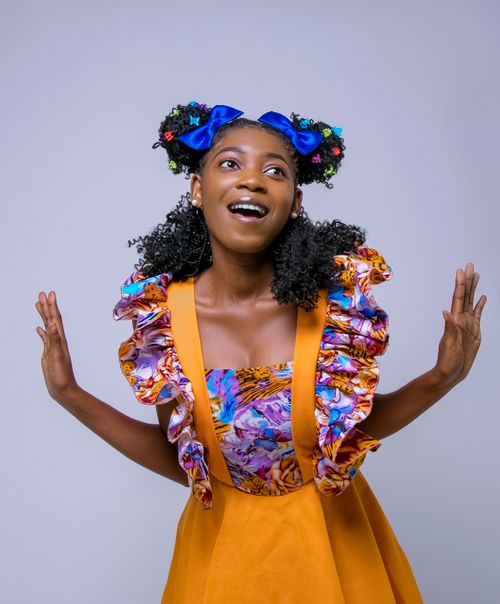 Free A vibrant young woman with curly hair and blue ribbons, wearing a floral dress. Stock Photo