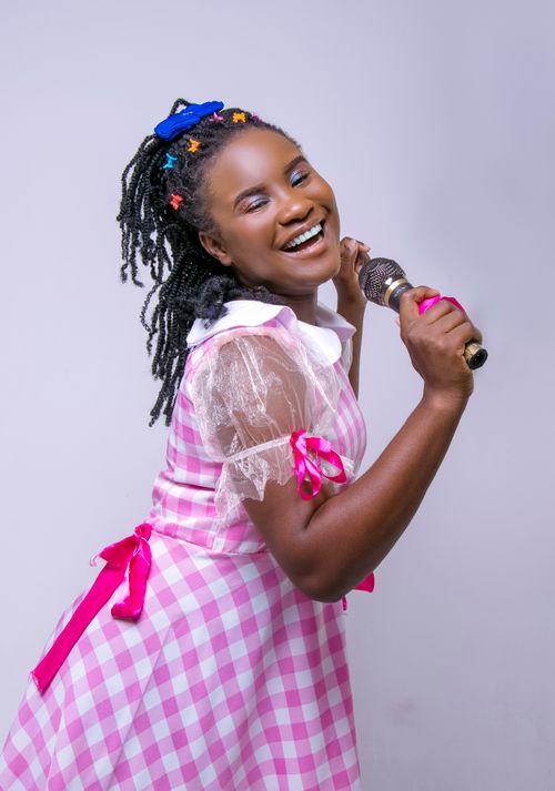 Free A cheerful woman in a pink dress sings while holding a microphone, expressing happiness and creativity. Stock Photo