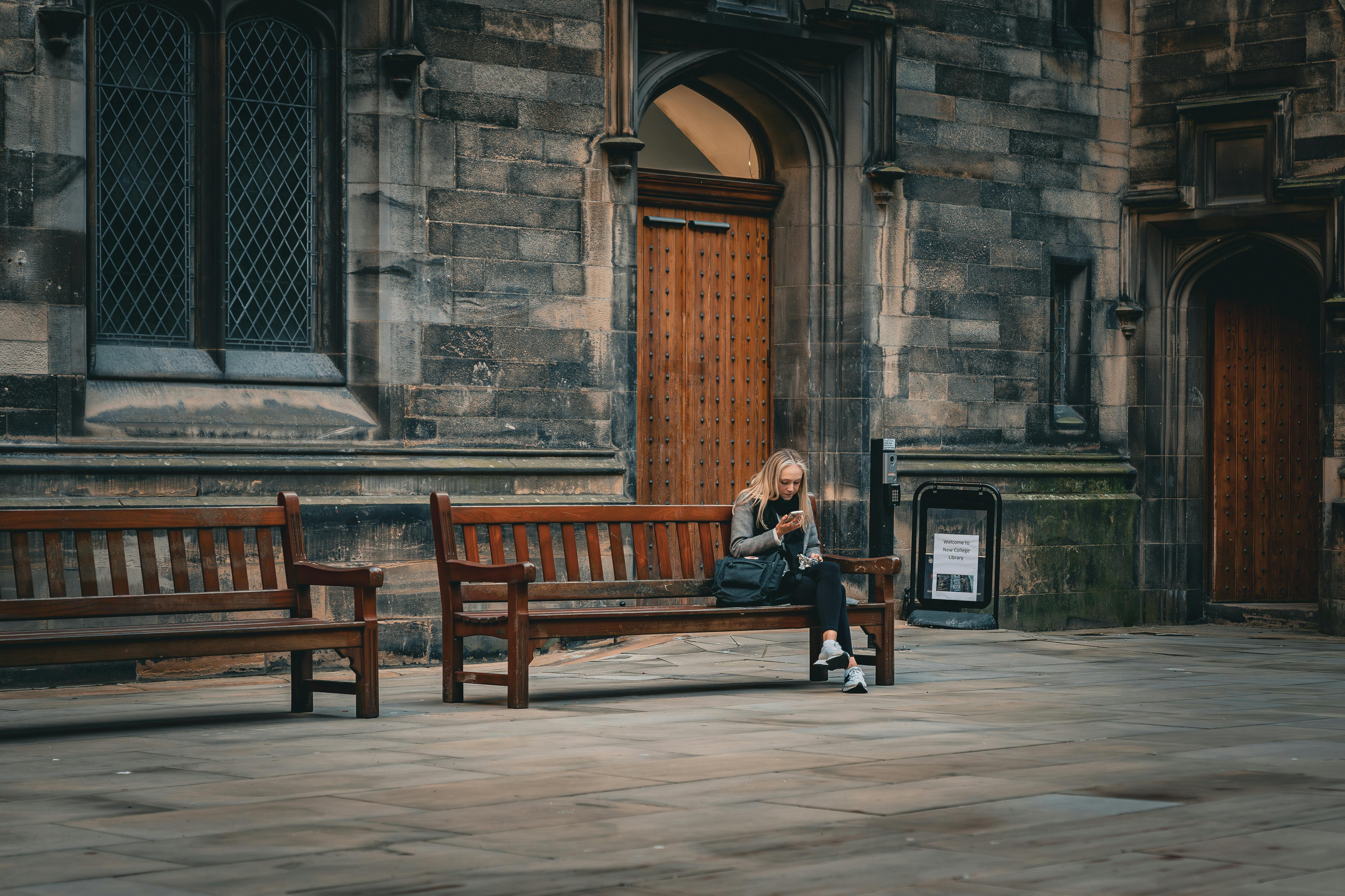 A woman sits on a bench reading in front of a historic building at Edinburgh University.