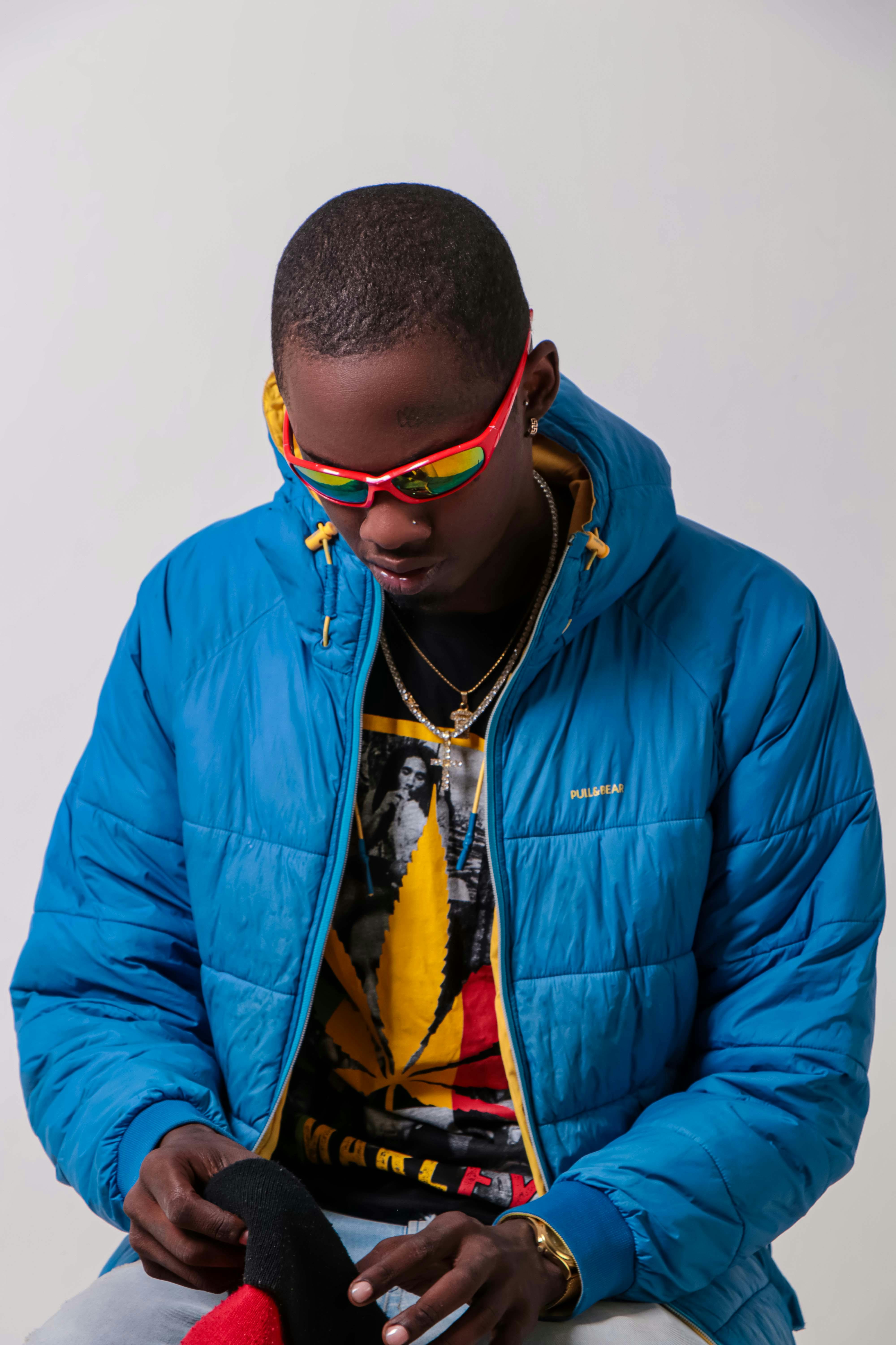 Fashionable young adult wearing a blue jacket and red sunglasses indoors.
