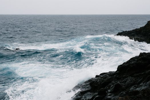 Dramatic ocean waves crash on a rocky coastline, captured in a vibrant seascape scene.