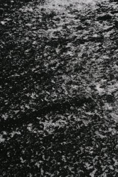 Close-up of a textured black surface with white patterns resembling foam or snow, perfect for abstract backgrounds.
