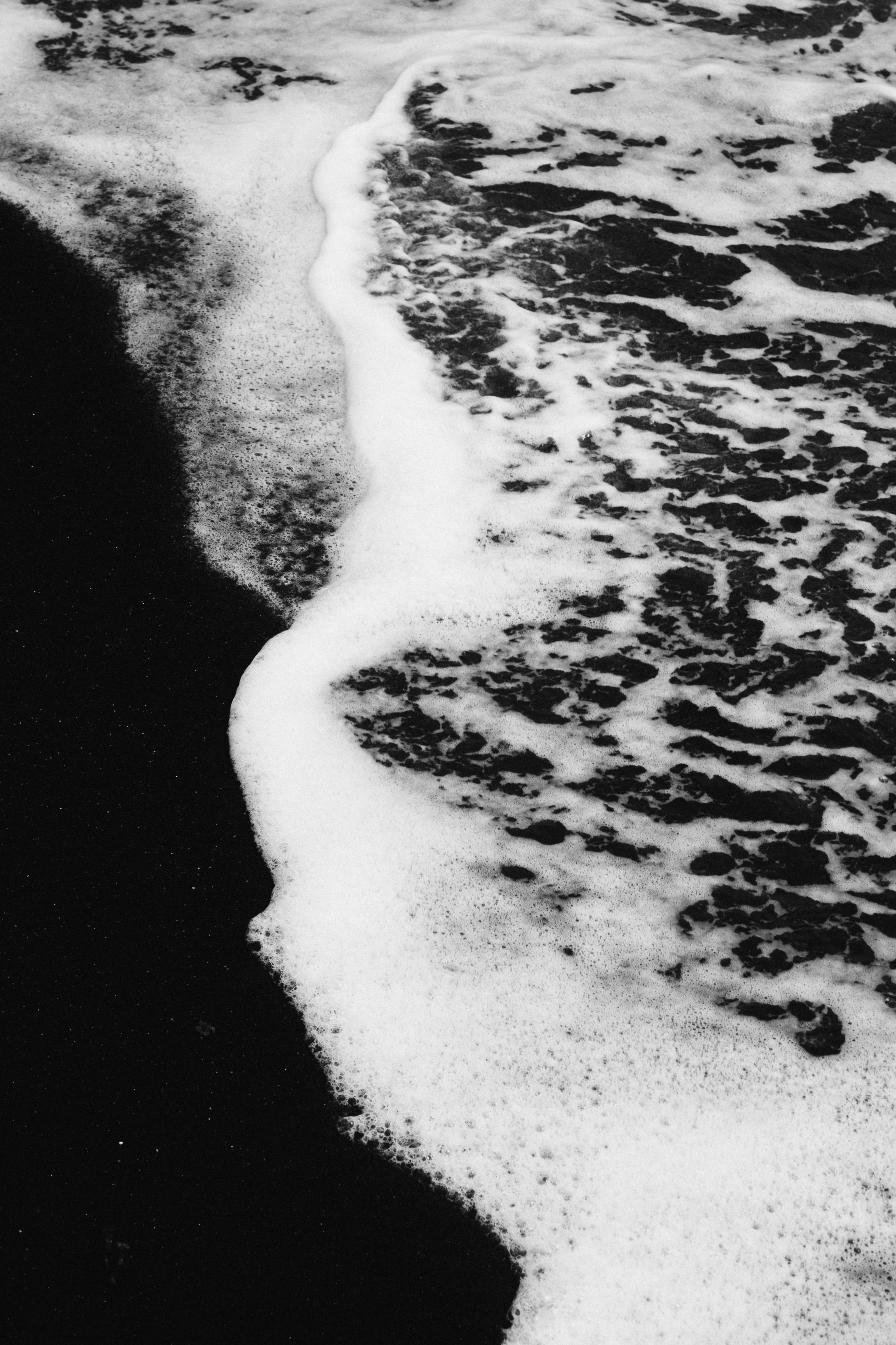 Black sand beach with ocean waves. Captures serene edge of water in monochrome.
