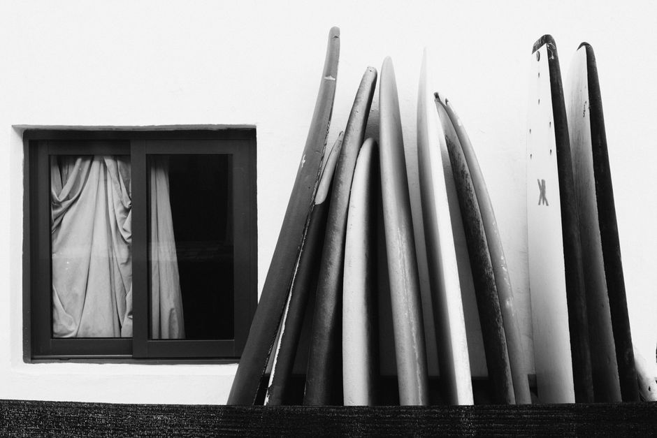 A collection of surfboards leaning against a wall with a curtained window.