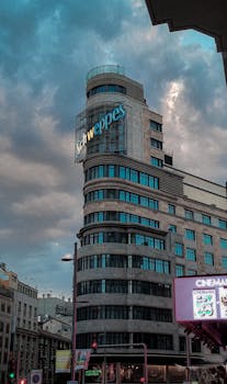 View of the iconic Capitol Building with Schweppes sign against a dramatic sky in Madrid.