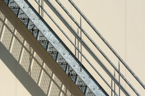 Free Abstract image of industrial metal stairs casting geometric shadows on a beige wall. Stock Photo