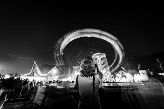 Black and white photo of a lively fairground at night with a spinning ride, capturing festive energy.