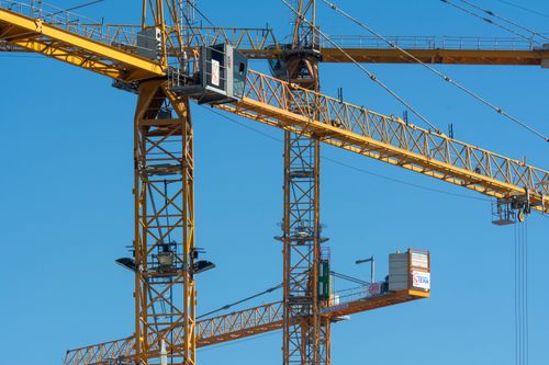 Free Close-up of industrial tower cranes operating against a clear blue sky, showcasing construction technology. Stock Photo