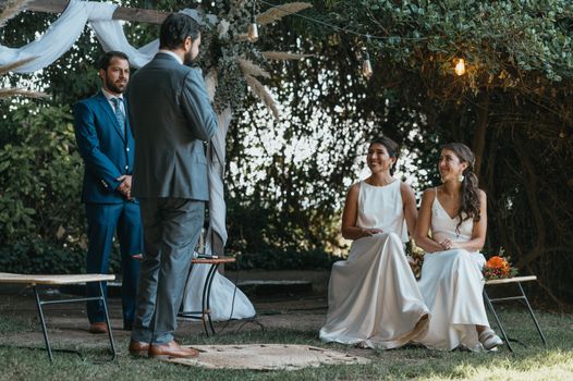 Two brides in elegant dresses enjoy an outdoor wedding ceremony.