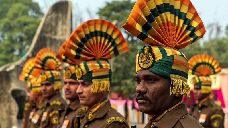 Indian soldiers in ceremonial uniforms with ornate headdresses standing outdoors.