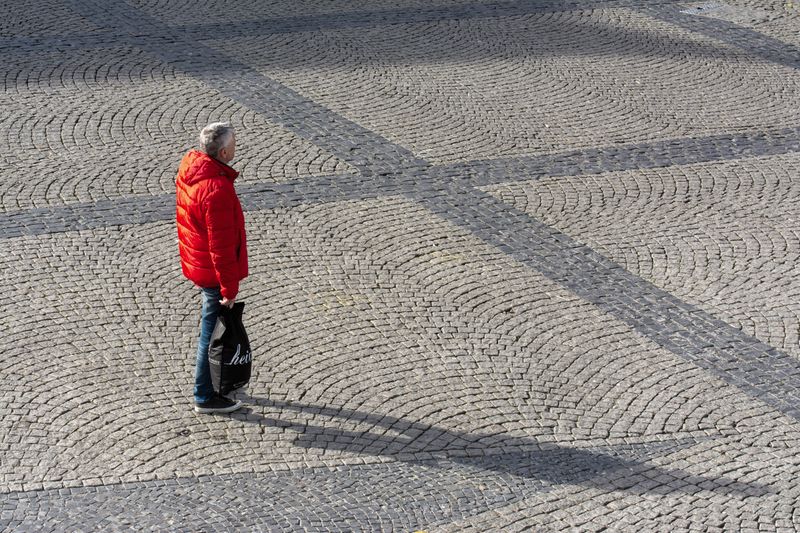Man in red jacket walking on patterned stone pavement in daylight.