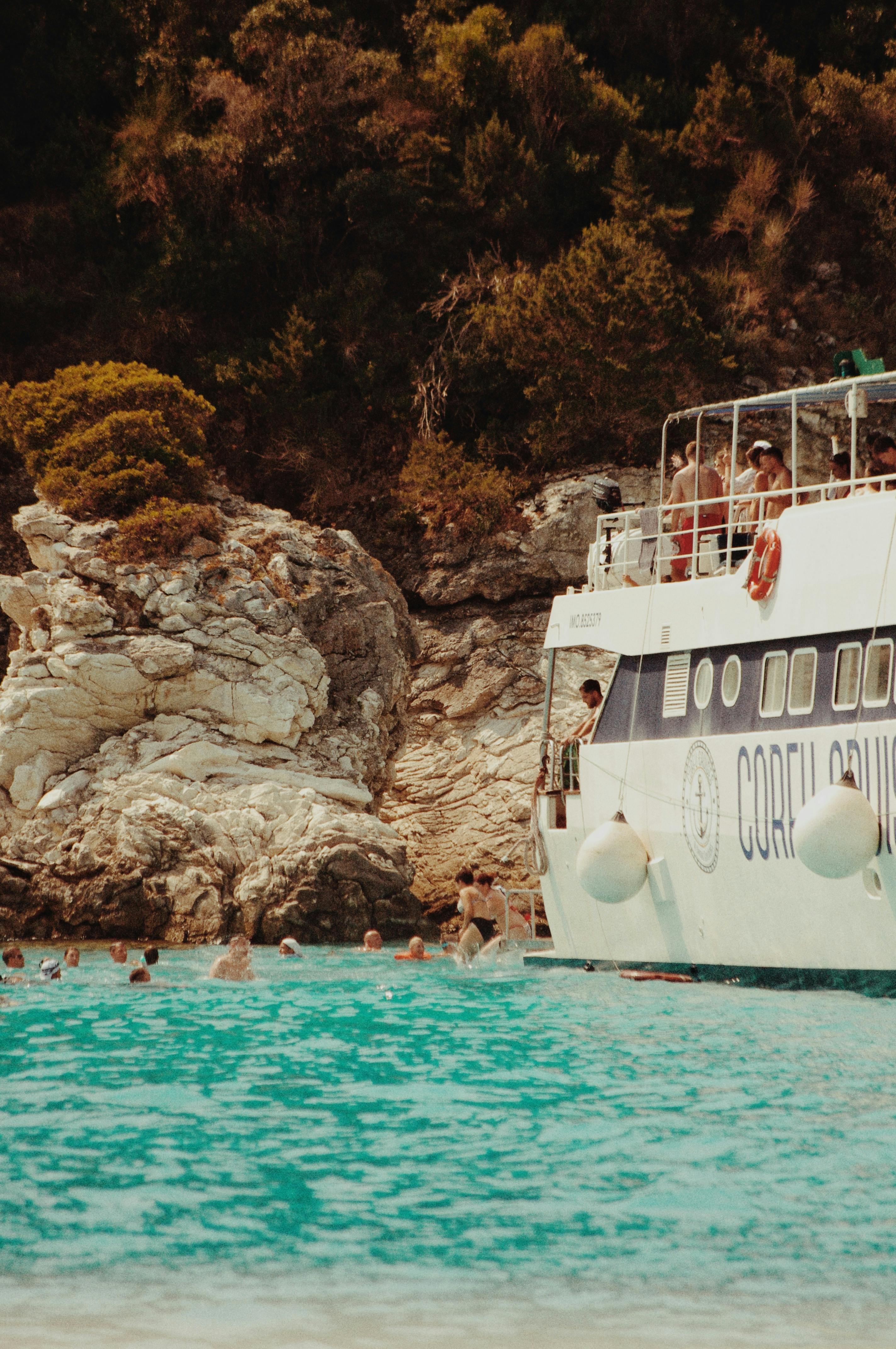 Beautiful cruise ship near the rocky coast of Paxos, Greece, with clear turquoise waters and lush greenery.