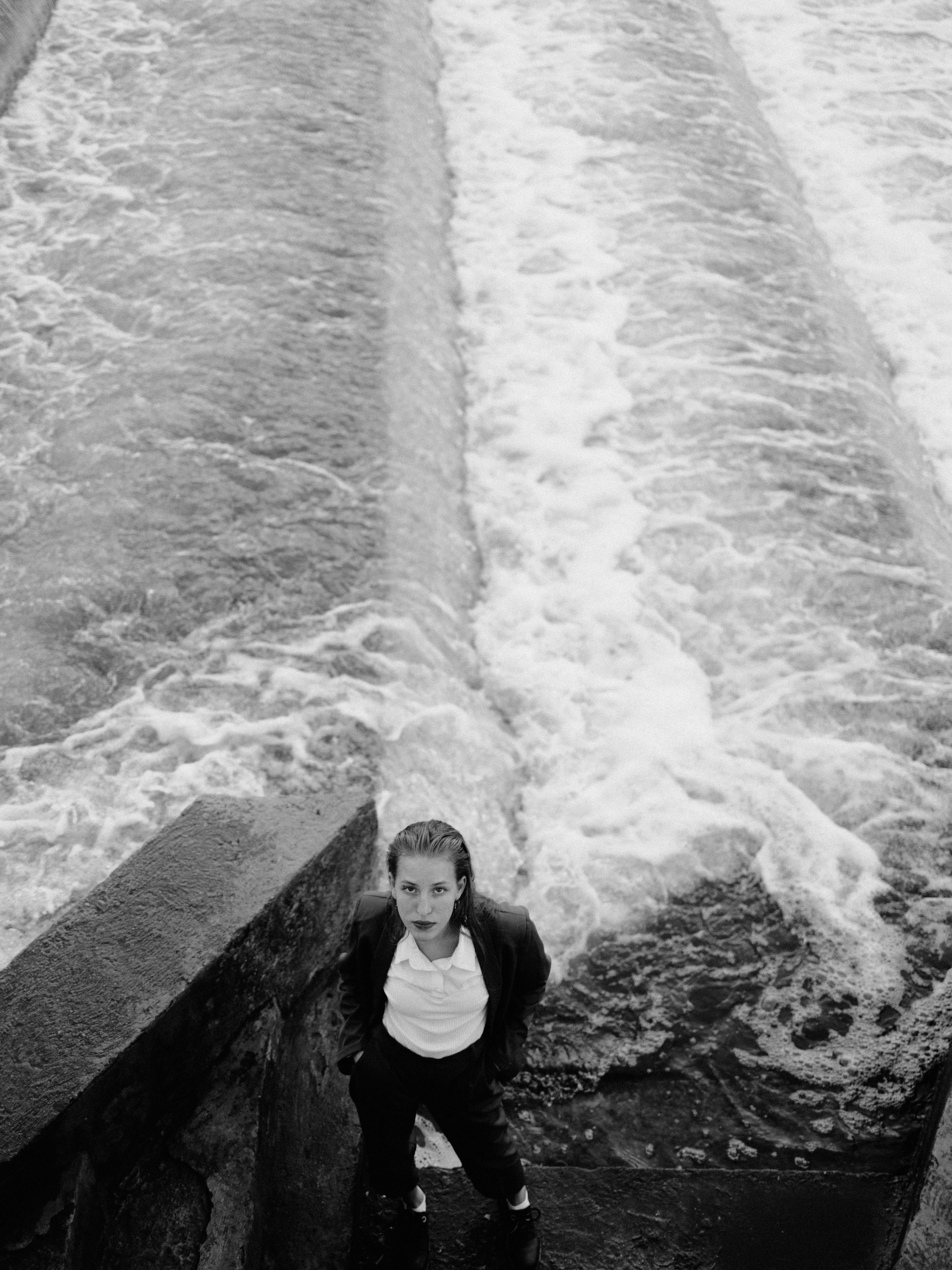 Moody black and white portrait of an adult by a flowing river.