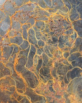 Close-up of an abstract pattern formed by rust on a metal surface with intricate lines and rich earthy colors.