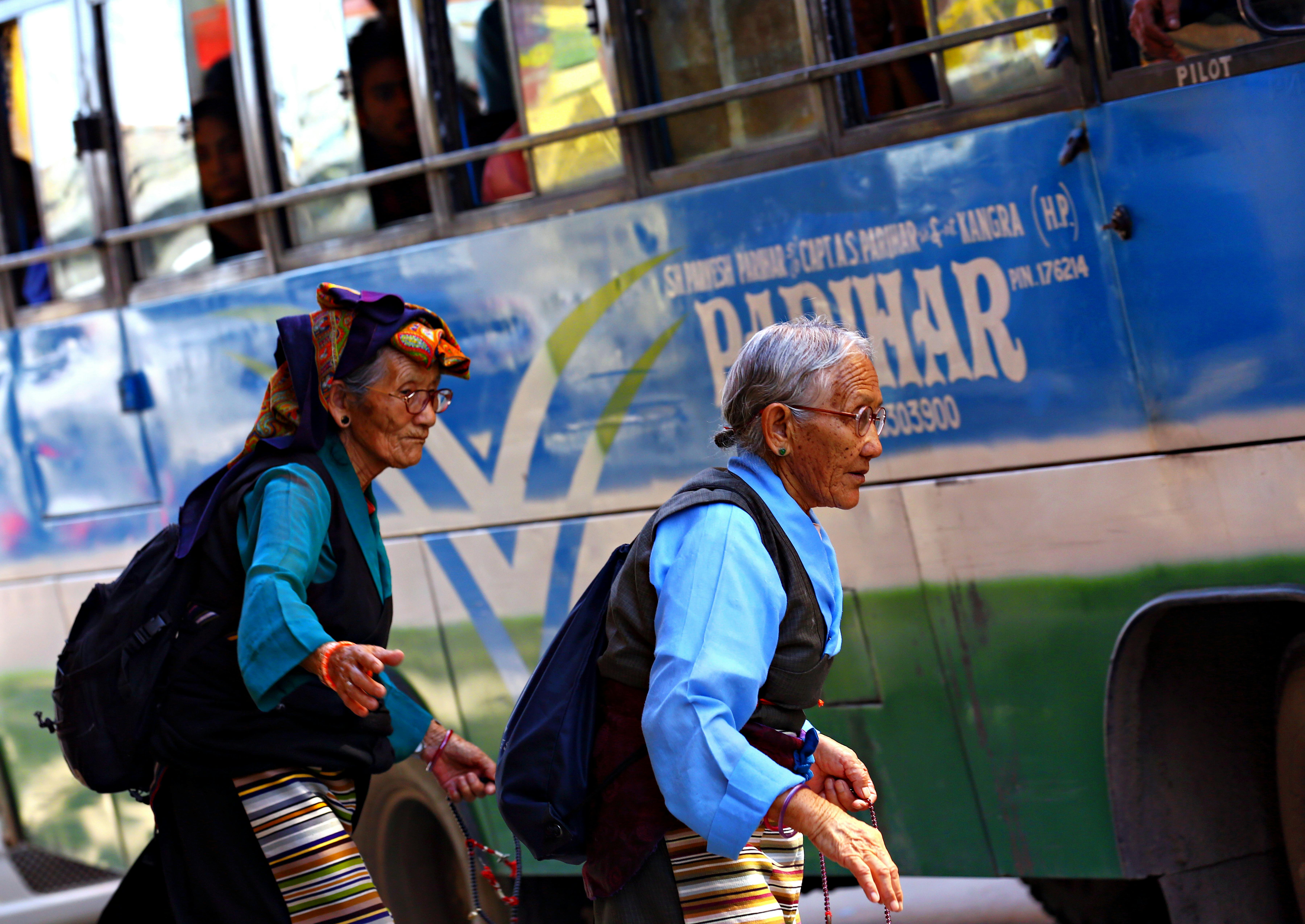 Two elderly women in traditional attire crossing the street near a local bus.