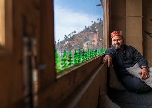 Free A man wearing a traditional hat relaxes by a window with mountains in the background. Stock Photo