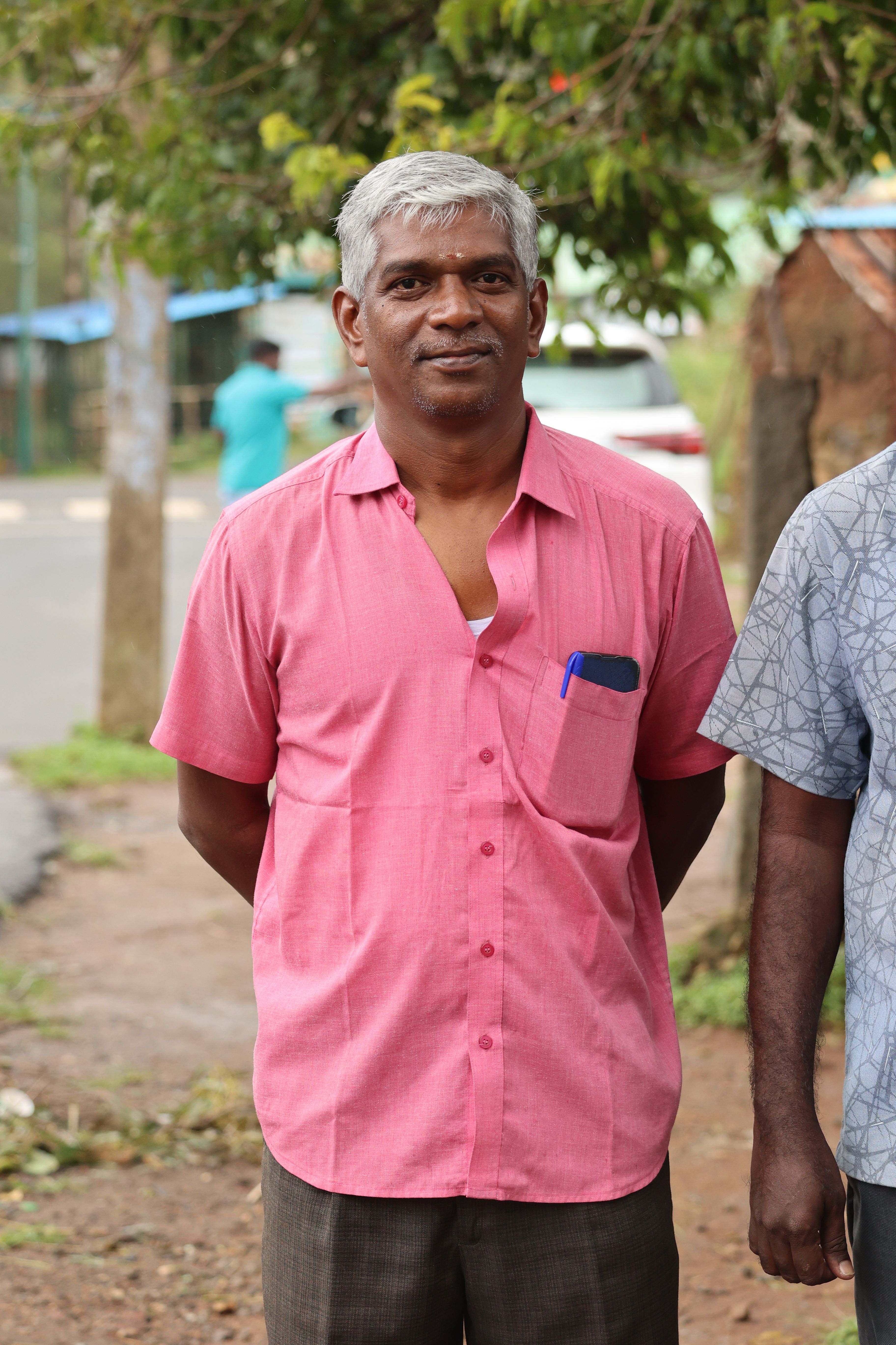 Mature man standing confidently outdoors in casual pink shirt.