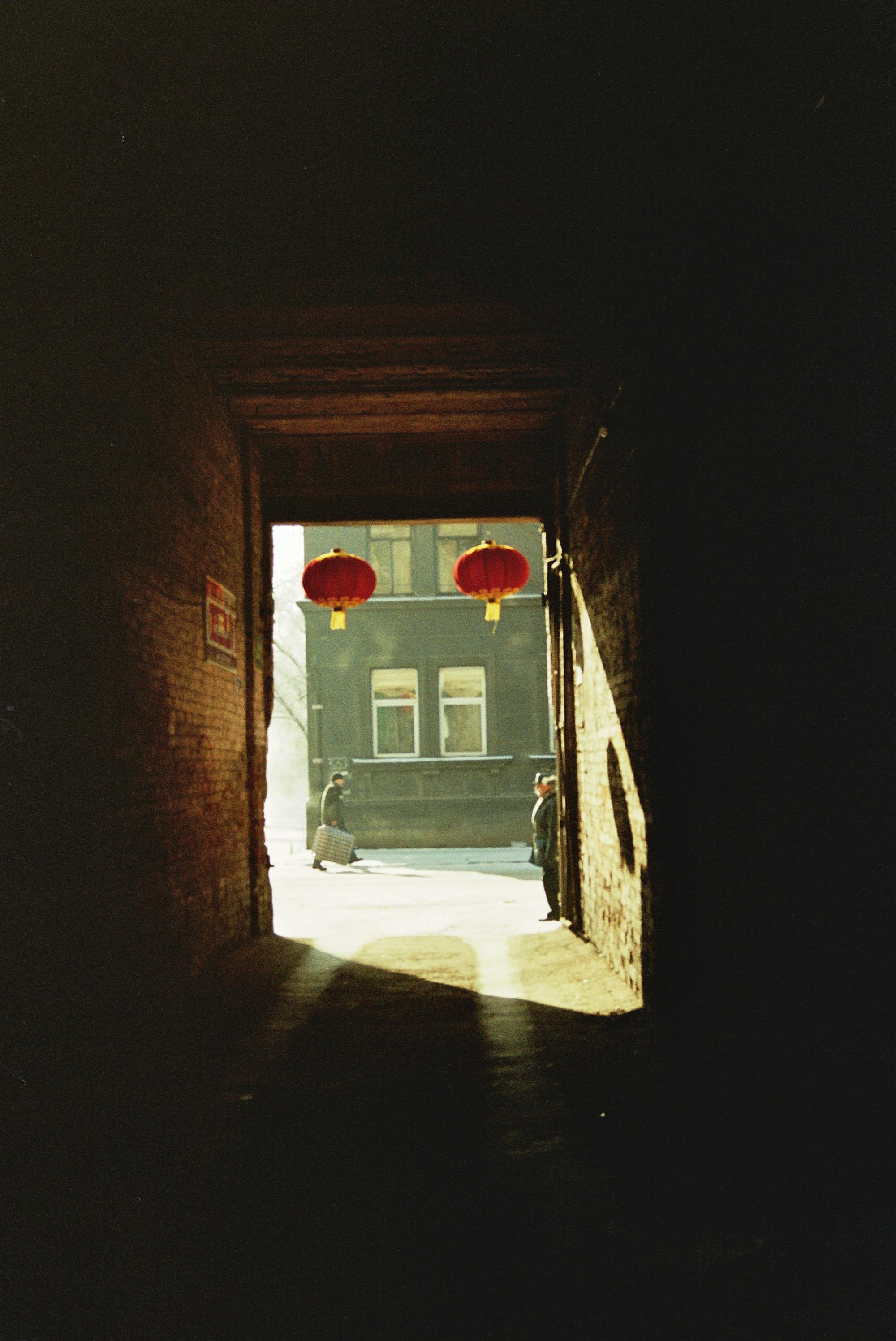 Free A mysterious alley with sunlight casting shadows and iconic red lanterns hanging. Stock Photo
