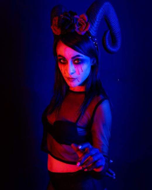 Mysterious woman in Gothic costume with horns under vibrant lighting, captured in Mexico City.