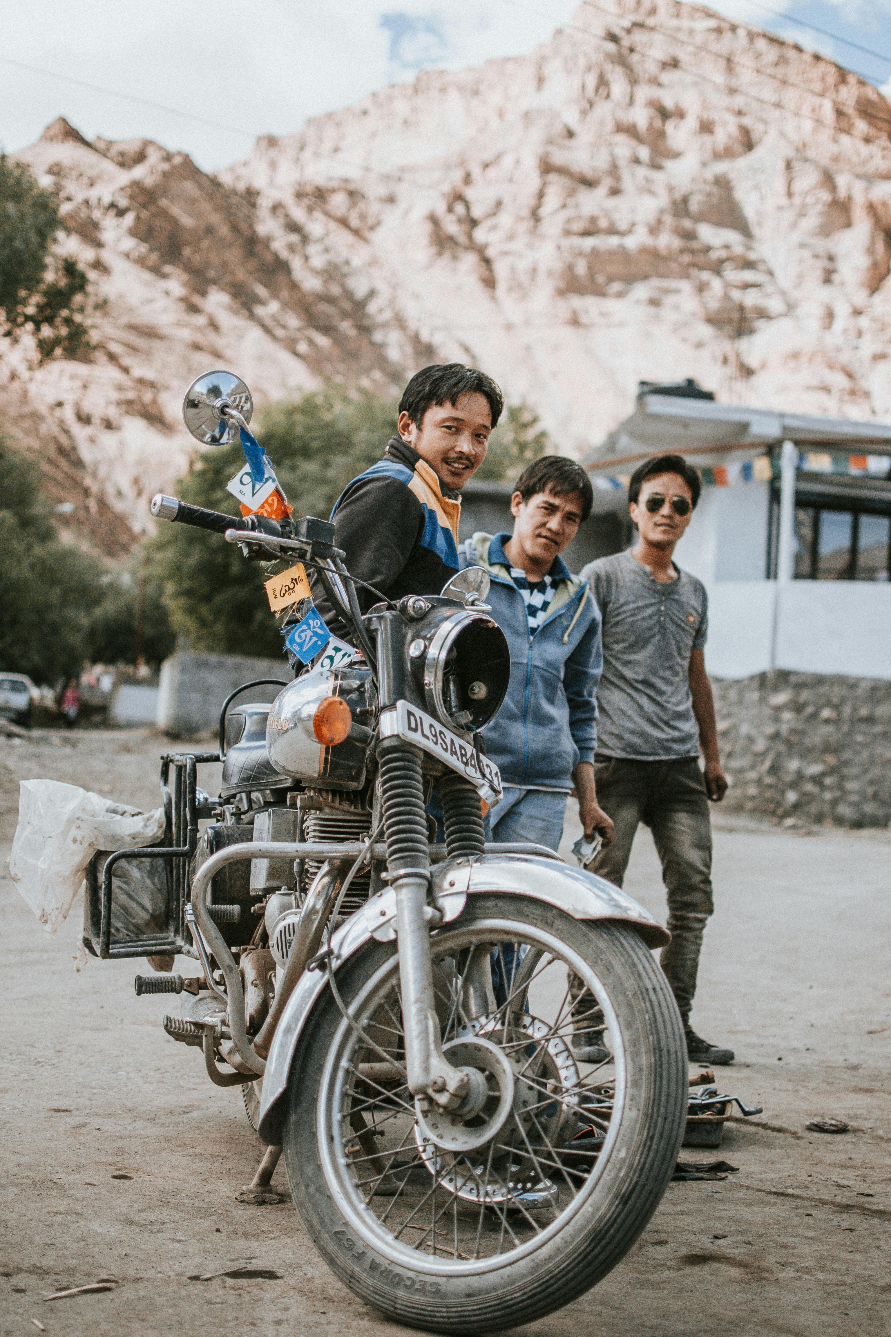 Three young men stand beside a classic motorcycle in a stunning mountainous region.