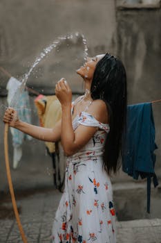 一位快乐的年轻女子穿着花卉连衣裙，在户外玩着软管，享受着夏日的乐趣