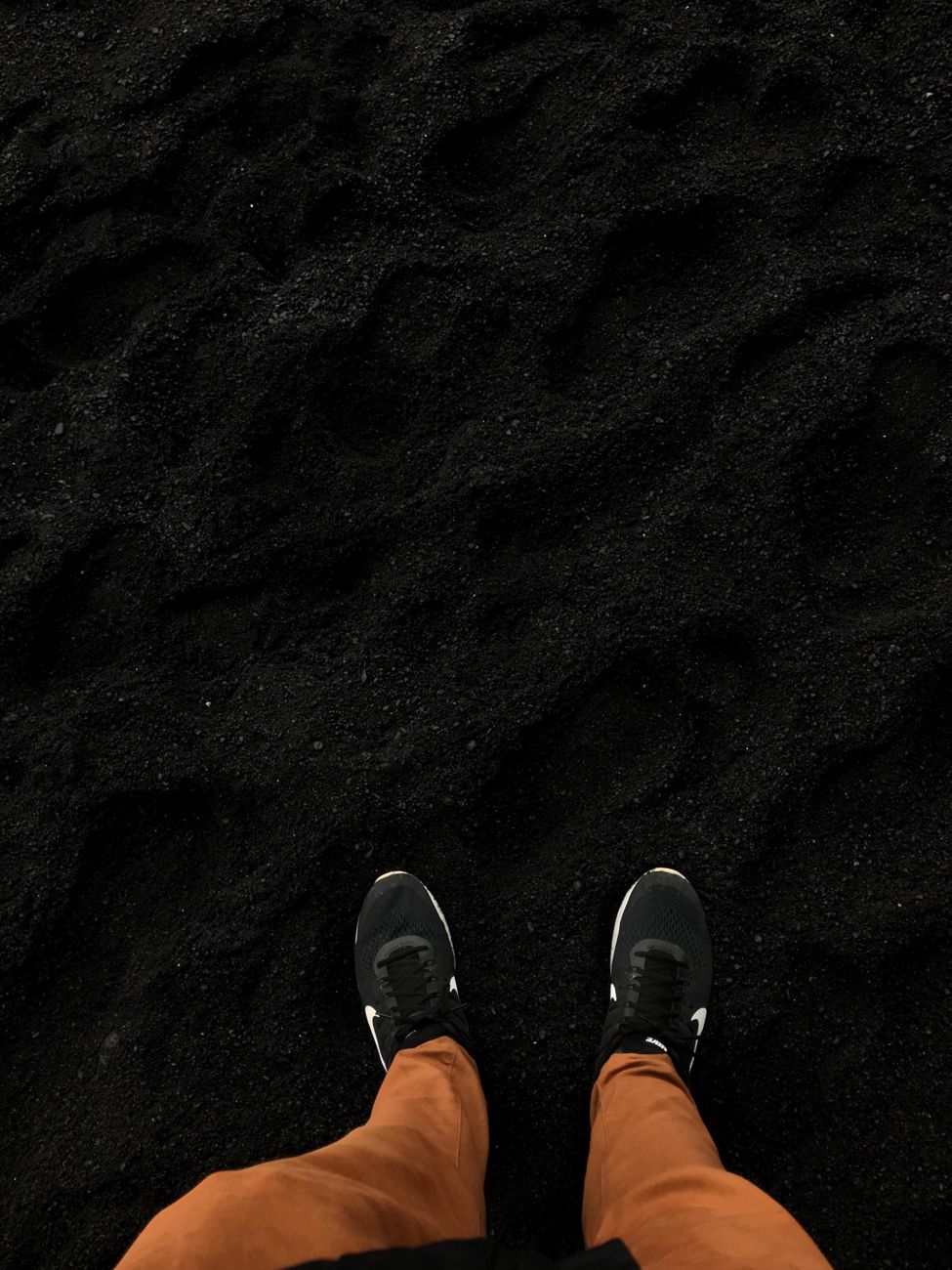 A person stands on a black sand beach in Iceland, wearing brown pants and sneakers.. pexels, person, stands