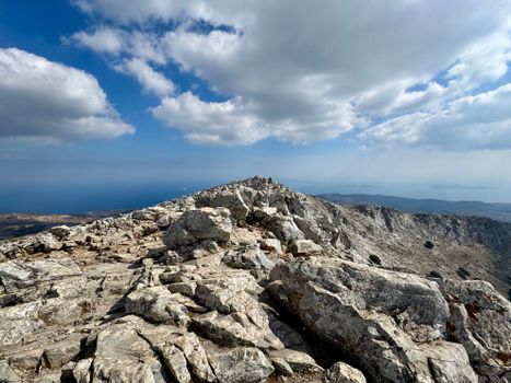 Rocky mountain peak under a bright sky with clouds, showcasing rugged terrain.
