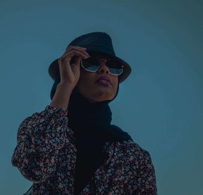 Fashionable woman outdoors in floral dress with sunglasses and hat, embodying elegance.