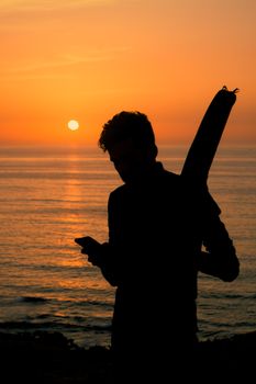 Silhouette of a man with a surfboard against a vibrant sunset over the ocean.
