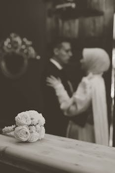 Black and white photo capturing a romantic indoor wedding moment with a bridal bouquet in focus.