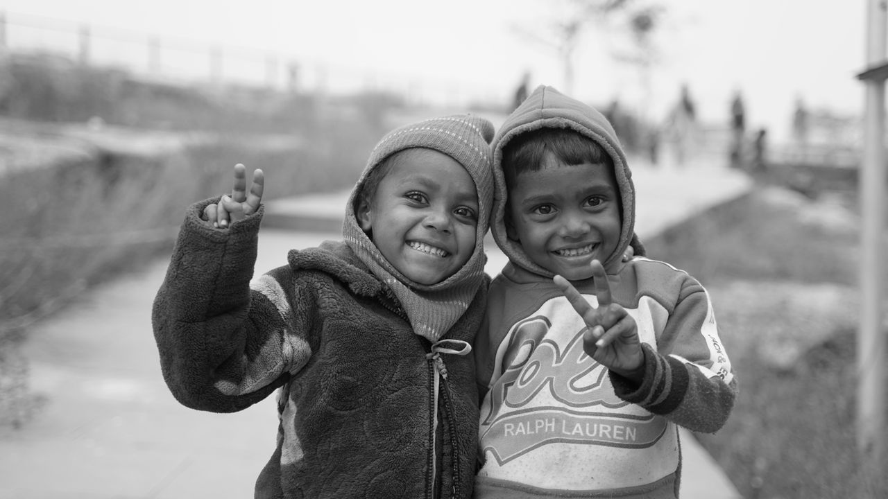 two smiling children in warm clothing making peace signs outside displ