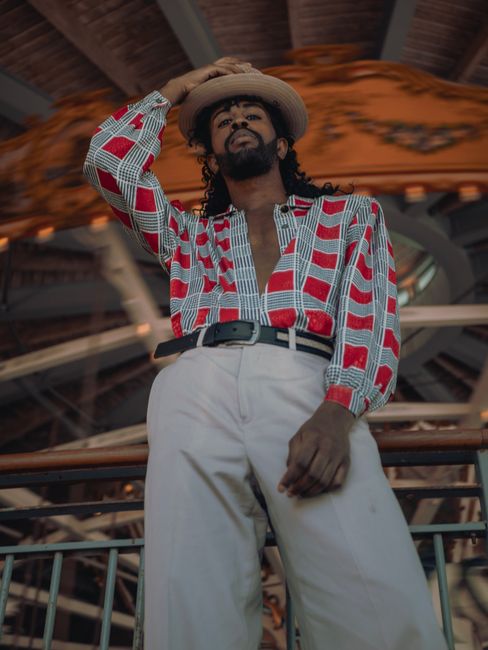 A fashionable man poses with a confident expression in a vibrant setting.