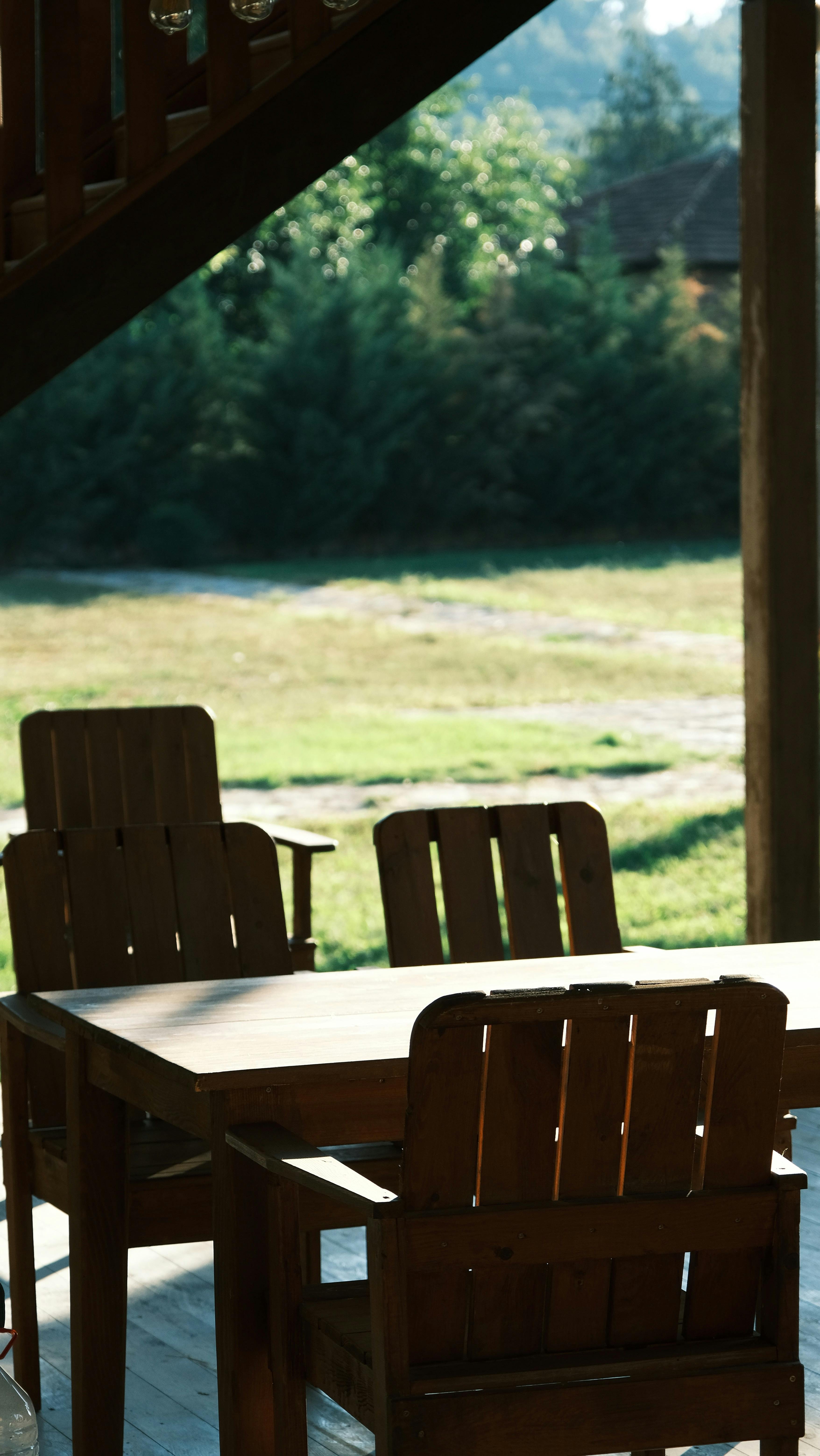 A tranquil outdoor patio with wooden chairs and table under lush greenery.