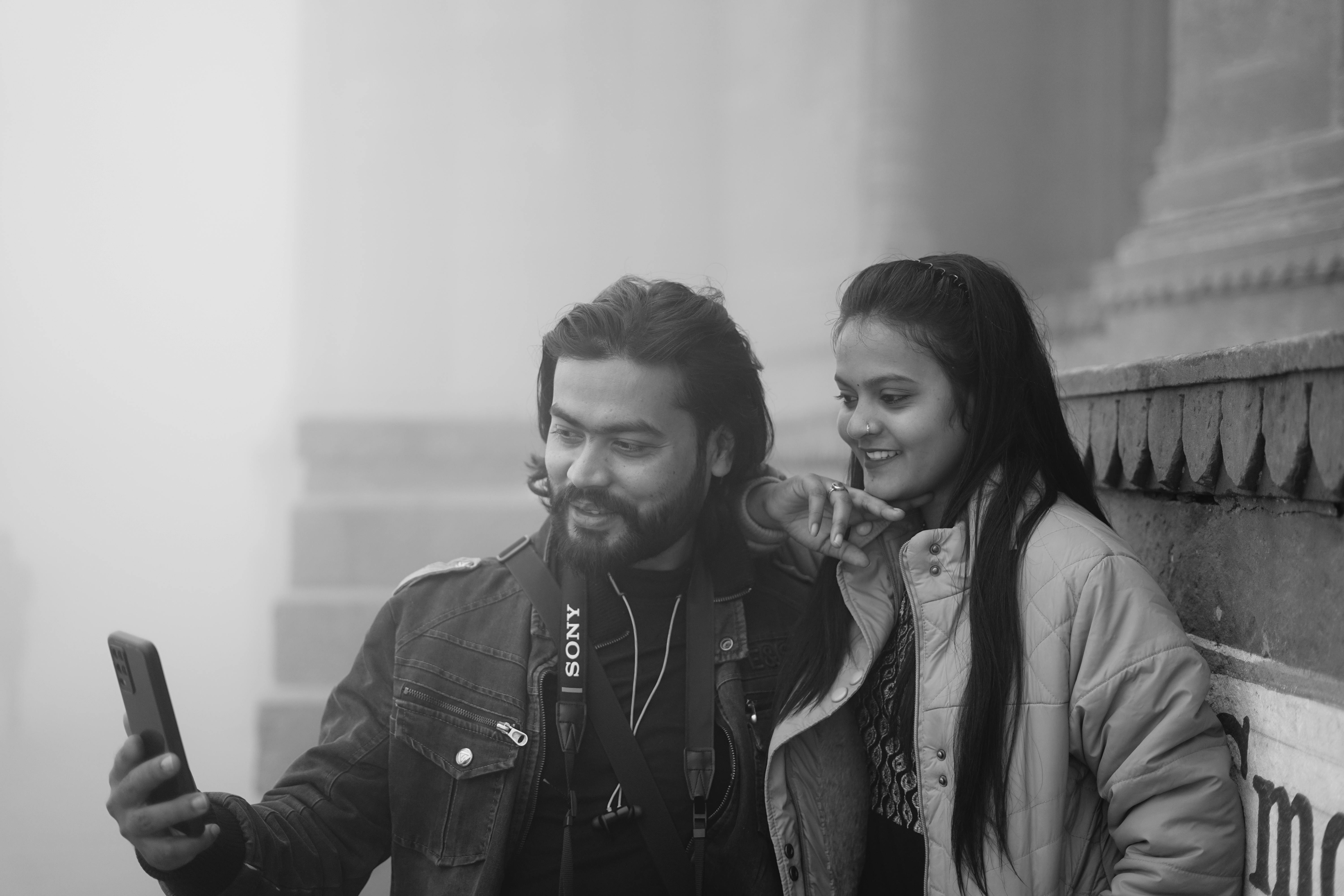 A young couple takes a selfie amidst foggy urban architecture, creating a serene atmosphere.