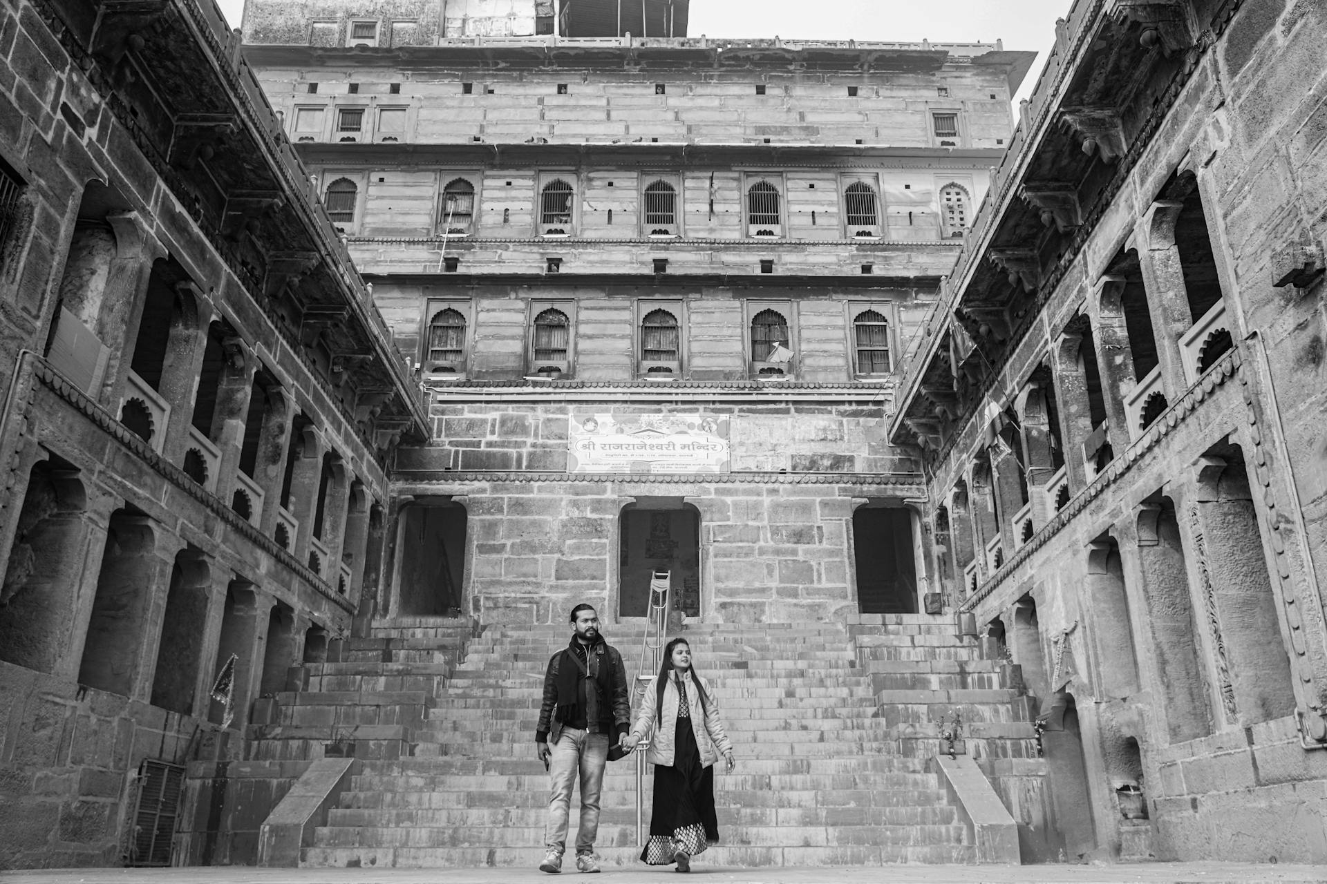 Couple walking through ancient Indian fort with intricate stone architecture. Black and white photo.