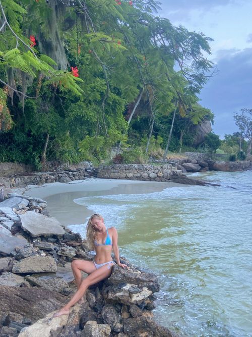 Free Basking in Tropical Serenity: A Woman Stands by the Shore, Embracing the Peaceful Harmony of Nature, the Warm Breeze, and the Gentle Ocean Waves.” Stock Photo