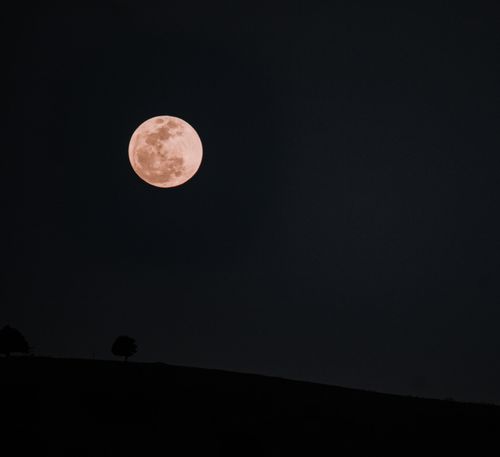 Free A tranquil full moon shines brightly over a dark silhouetted landscape, creating a serene night scene. Stock Photo