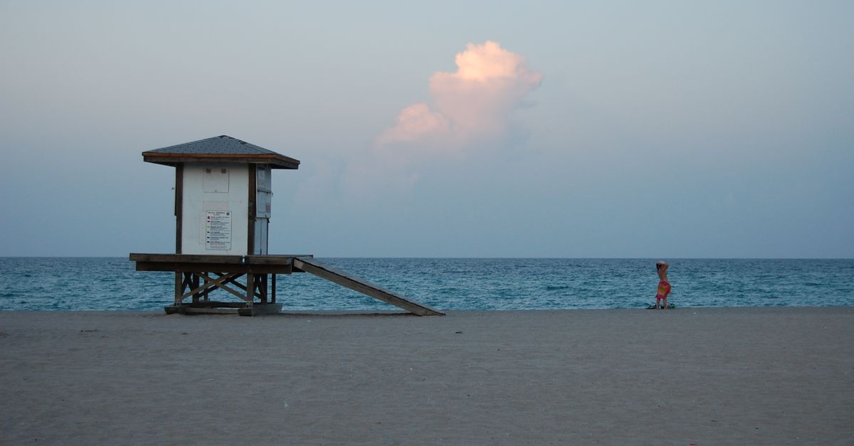 A serene Miami Beach scene featuring a lifeguard tower and a lone person at sunset.