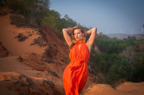 Free A woman in an orange dress poses in a desert landscape with wind turbines in the background. Stock Photo