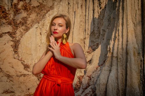 Free Stunning woman in vibrant orange dress posing outdoors against rock formations. Stock Photo