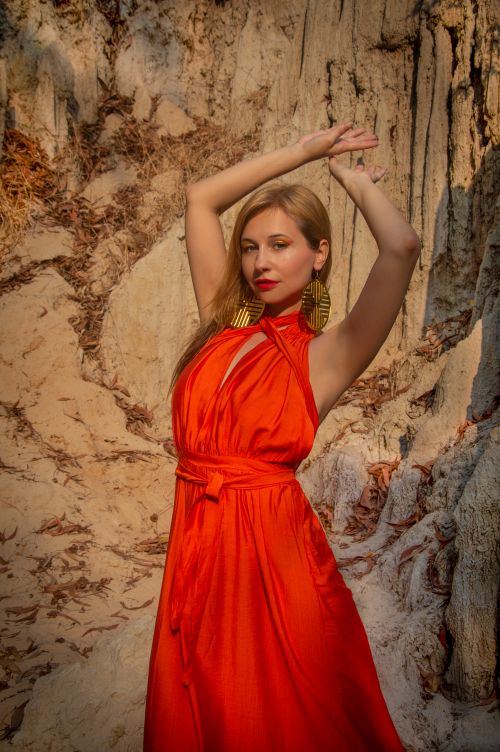 Free Stylish woman in a red dress posing against a textured rocky backdrop. Fashion-focused. Stock Photo