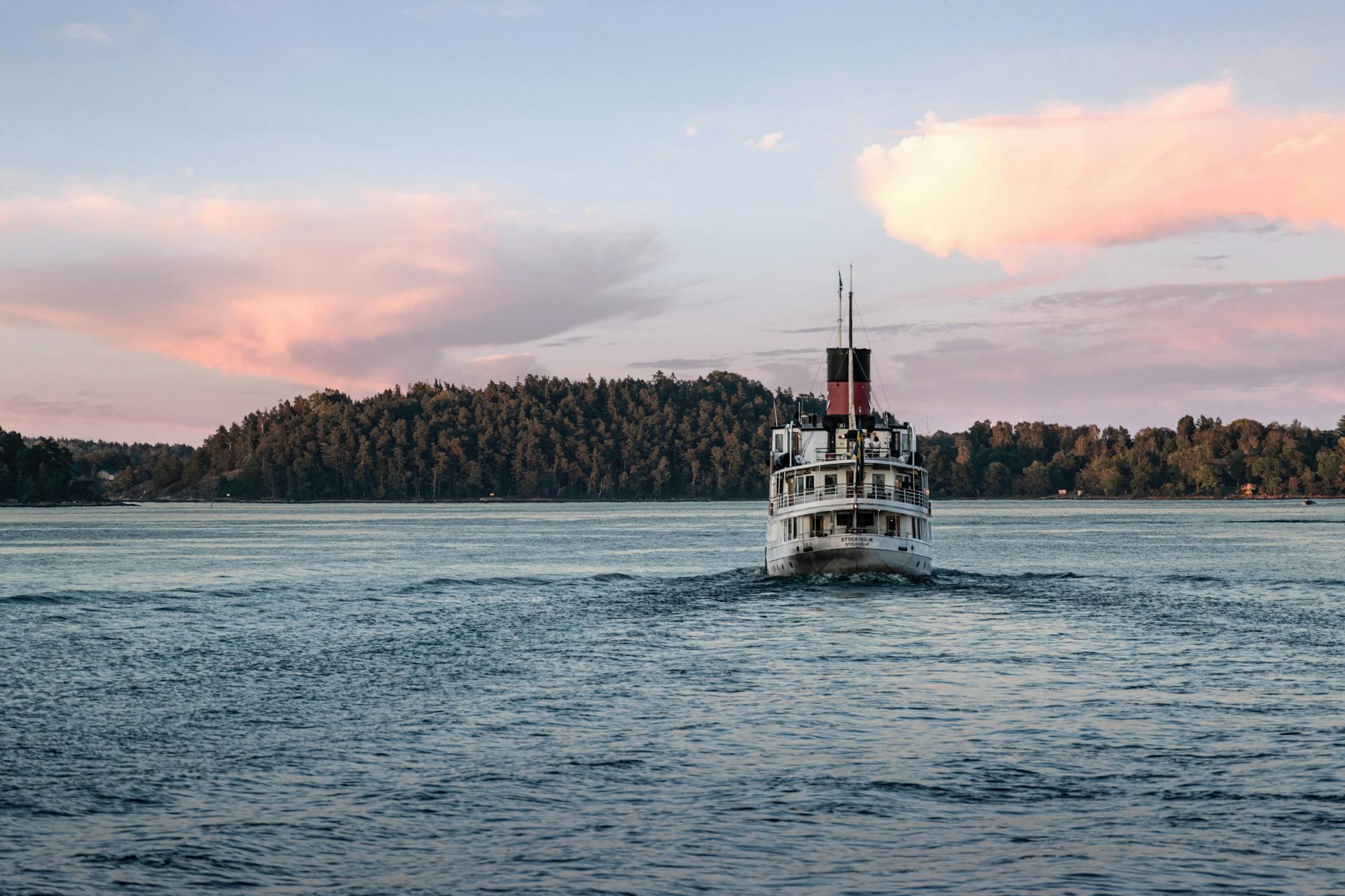 Historic steamboat cruising on a serene lake framed by a forested landscape under a colorful sunset sky.