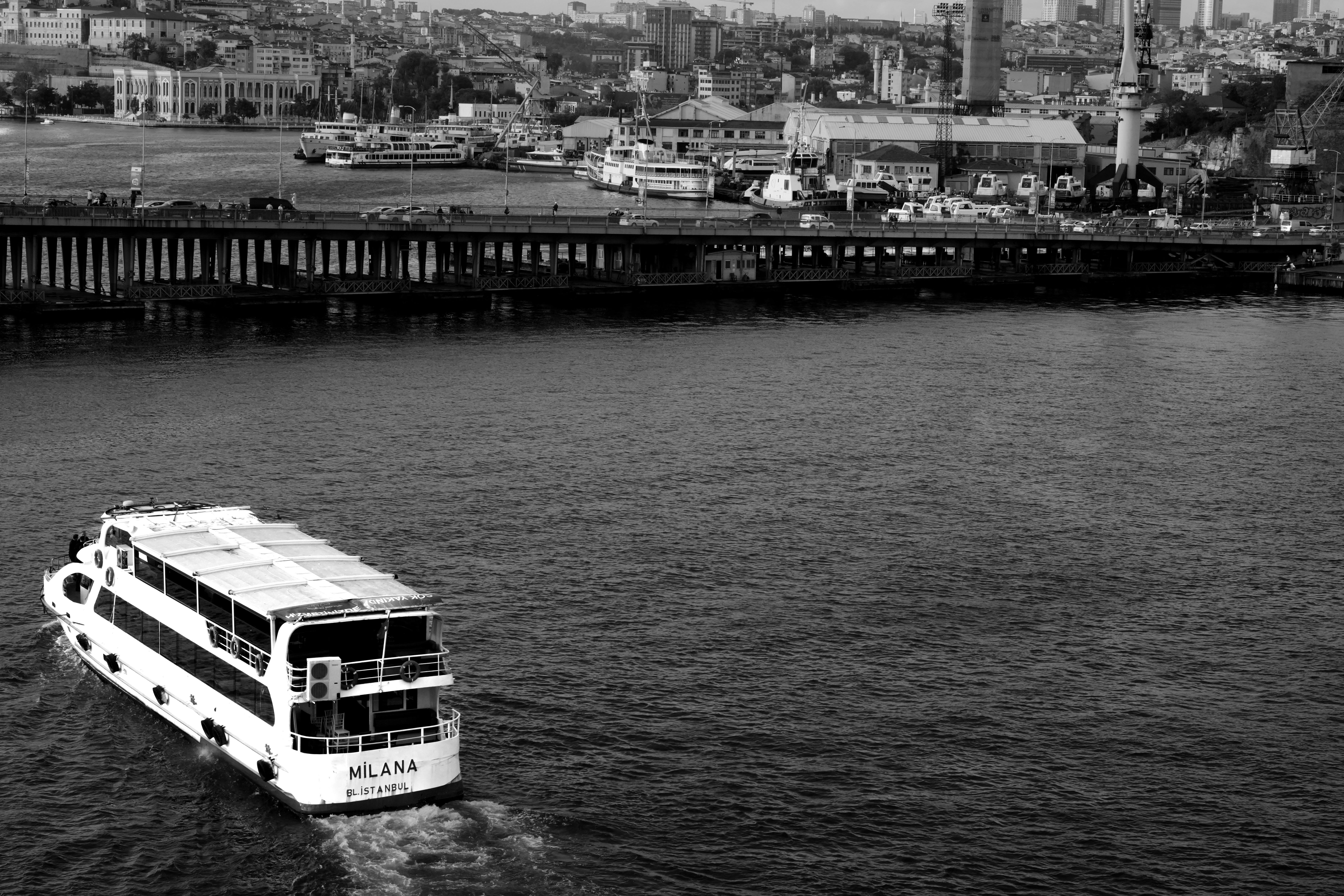 A black and white photo of a ferry cruising on the Bosphorus with Istanbul cityscape in the background.