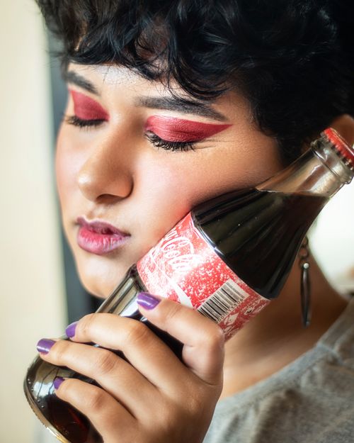 Free Close-up portrait of a woman with bold makeup holding a soda bottle, conveying a retro fashion vibe. Stock Photo