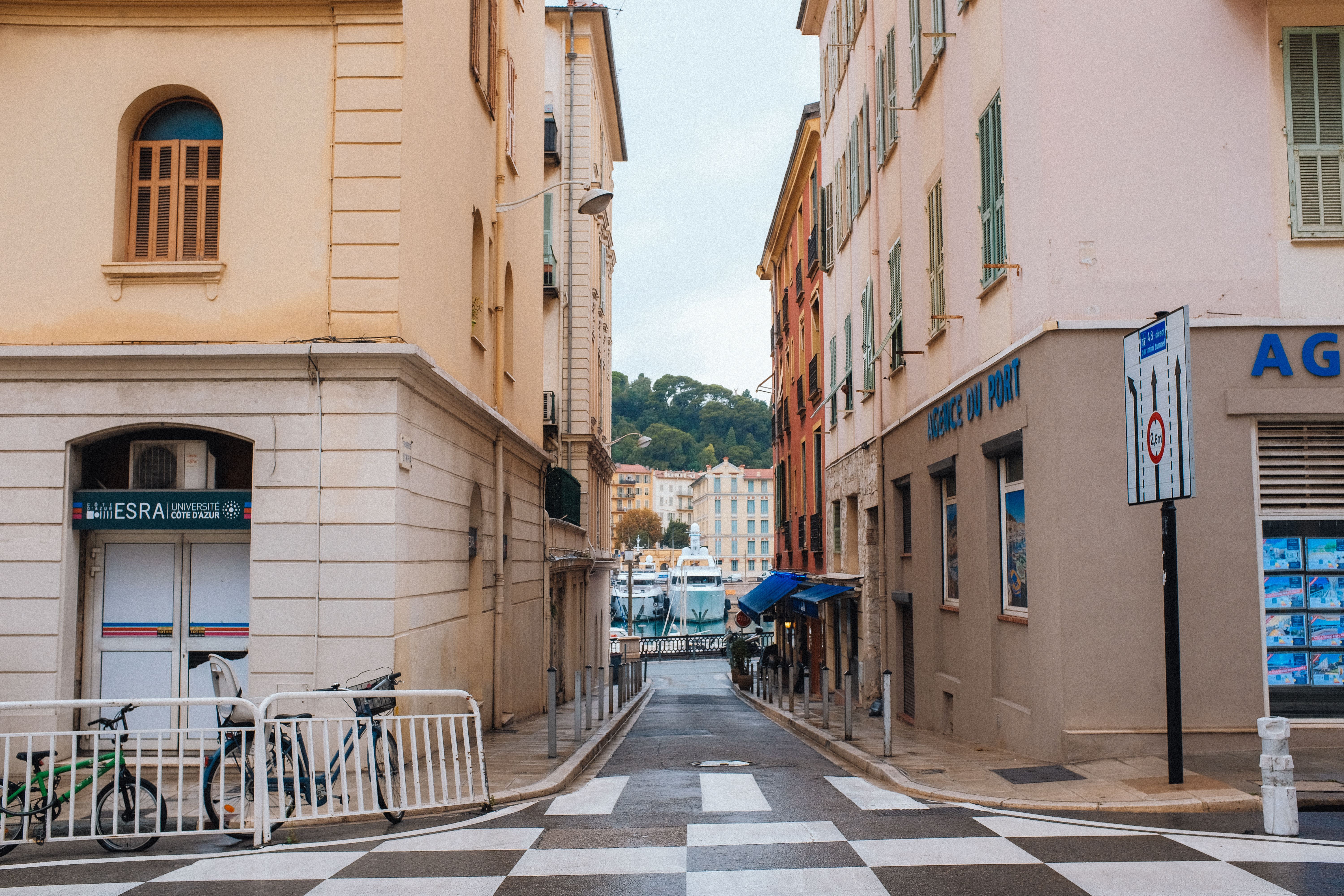 A picturesque street view in a European city leading to a lively port with boats.
