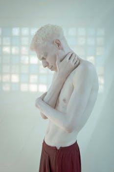Contemporary portrait of an albino man posing shirtless in a bright studio setting.