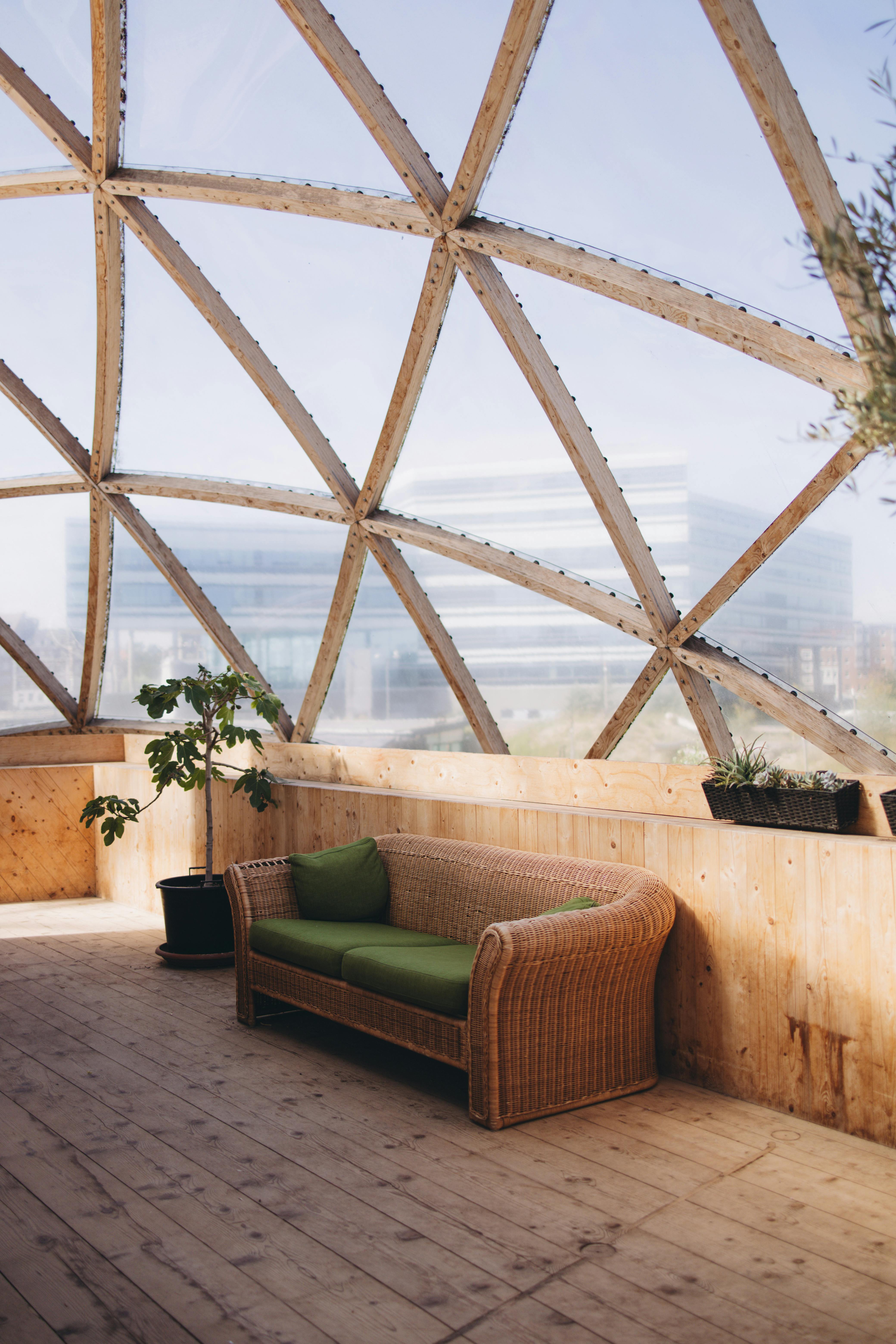 Cozy wicker couch in a glass dome interior with cityscape view.