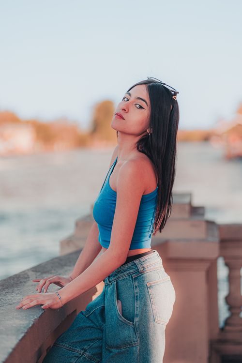 Free Fashionable young woman in casual attire posing by a river in a sunset setting. Stock Photo