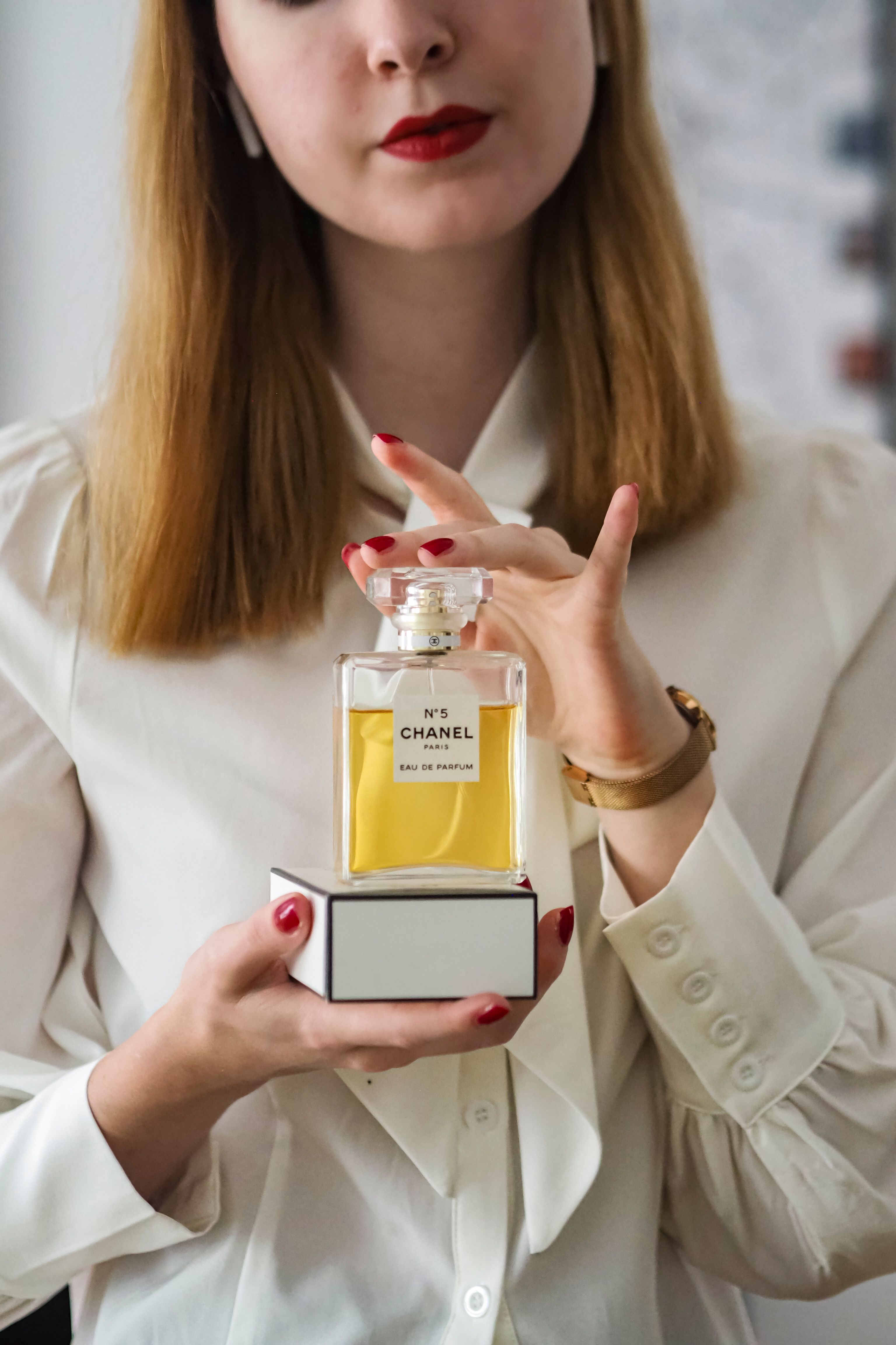Mulher chique em blusa branca exibindo o icônico frasco de perfume Chanel No. 5.